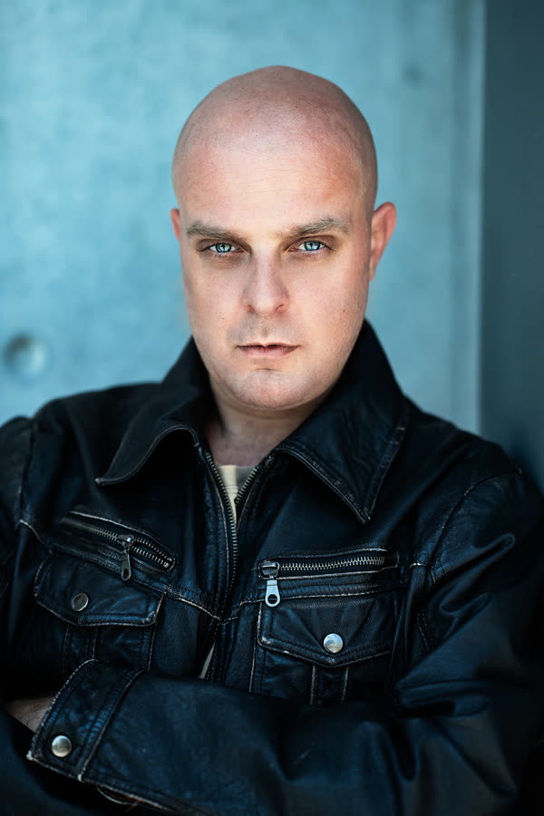 Manuel Köhler in a black leather jacket, arms folded, in front of a concrete wall